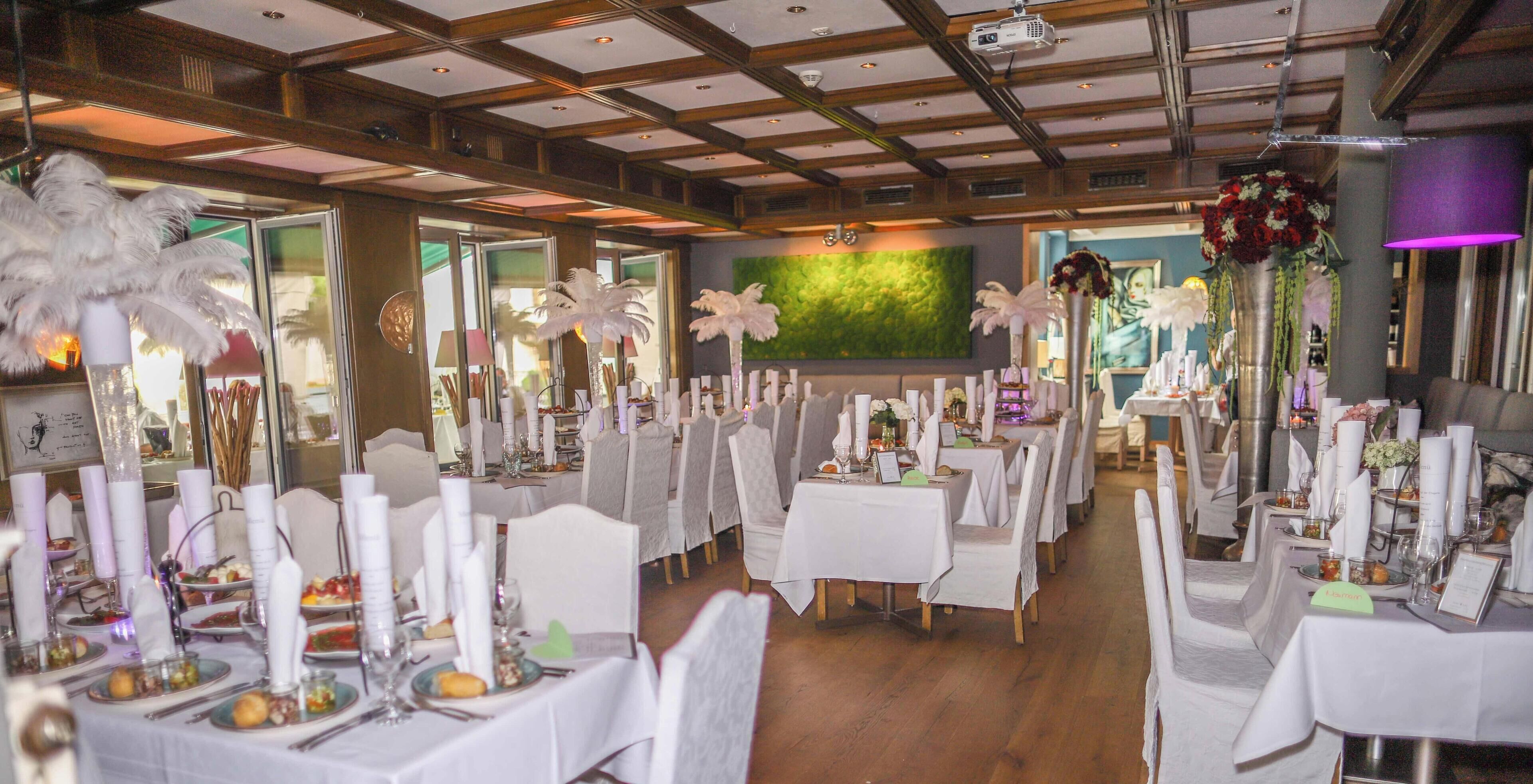 Un salón de banquetes con manteles blancos, centros de mesa con plumas y un mural de pared verde.