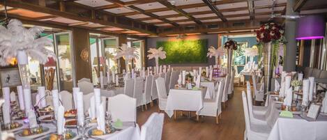 Un salón de banquetes con manteles blancos, centros de mesa con plumas y un mural de pared verde.