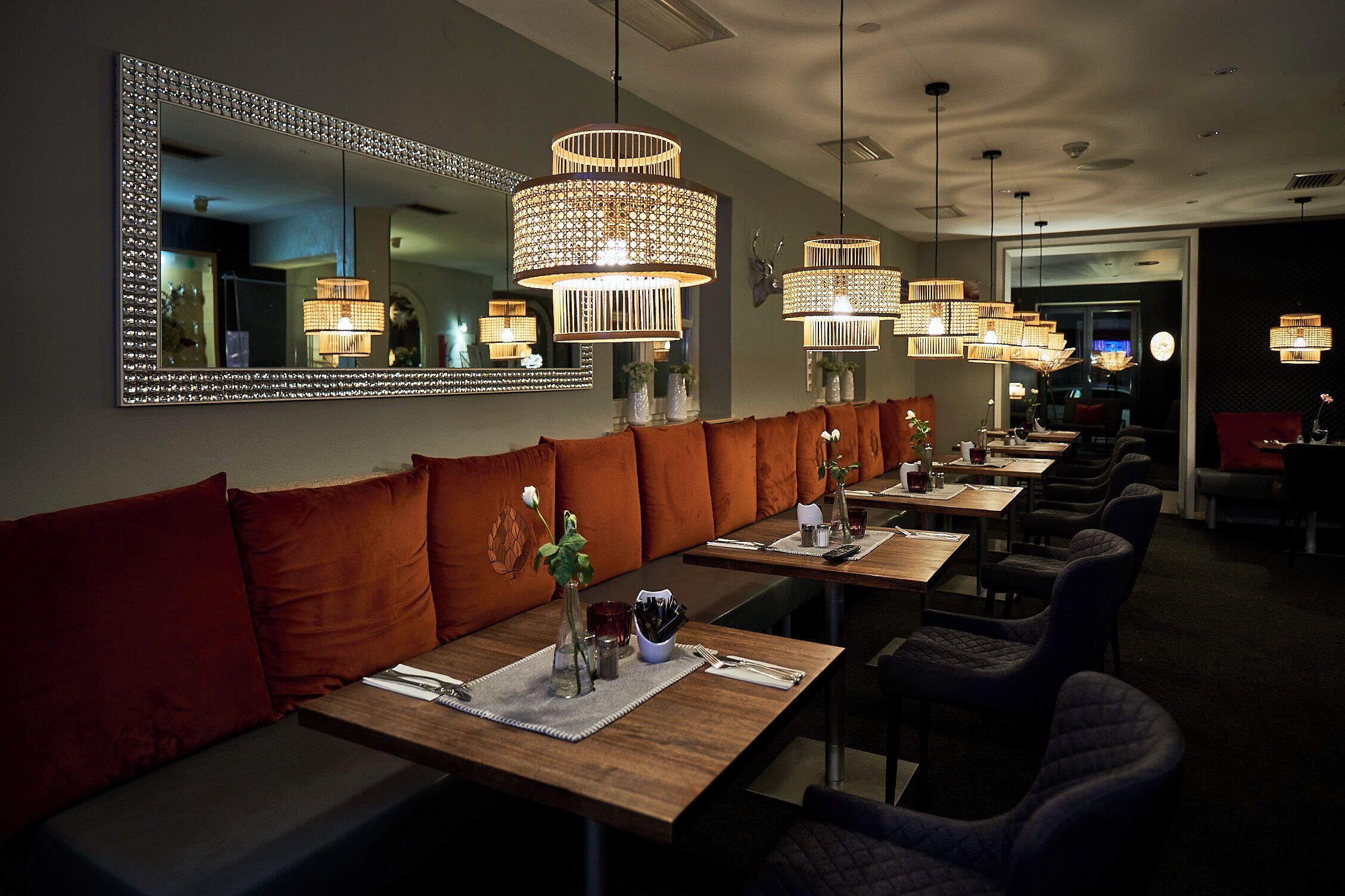 Un restaurant doté d’un long banc servant de siège, de plusieurs tables et de luminaires suspendus.