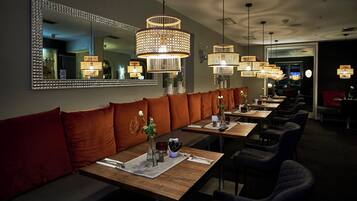 Un restaurant doté d’un long banc servant de siège, de plusieurs tables et de luminaires suspendus.