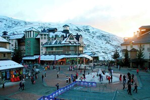 A snow-covered town square with buildings, including a prominent hotel with a green facade and a tower. - Modern Apartment Near the Slopes (Sierra Nevada)
