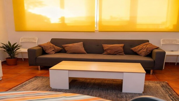 A modern living room with a grey sofa, multiple brown cushions, a wooden coffee table, and a large yellow artwork on the wall. - Snow covered Apartment in Sierra Nevada (Sierra Nevada)