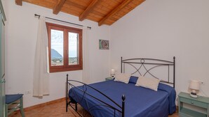 Un dormitorio con cama, una ventana con cortinas, una mesita de noche con lámpara y vistas al exterior.