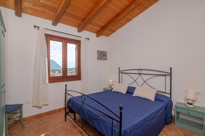 Una camera da letto con un letto, una finestra con tende e un comodino con una lampada, e vista sull'esterno.