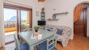 Una habitación con una mesa de comedor, sillas, un sofá, un televisor, una planta y vistas a través de un ventanal.