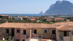 Un pueblo costero con casas de tejados terracota, una montaña imponente al fondo y una vista despejada del mar.