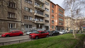 Straßenansicht mit parkenden Autos und mehrstöckigen Gebäuden, von denen einige mit Graffiti versehen sind.
