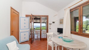 A room with a dining table, chairs, a sofa, a TV, and a view of the sea through a glass door. - Villetta Oleandro with Sea View, Private Terrace and Garden (San Teodoro)