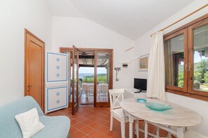 A room with a dining table, chairs, a sofa, a TV, and a view of the sea through a glass door. - Villetta Oleandro with Sea View, Private Terrace and Garden (San Teodoro)