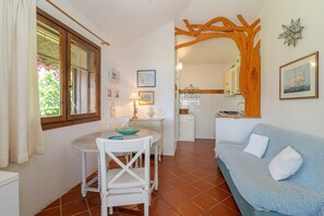 A cozy living room with a dining table, a sofa, and a kitchen in the background. - Villetta Oleandro with Sea View, Private Terrace and Garden (San Teodoro)