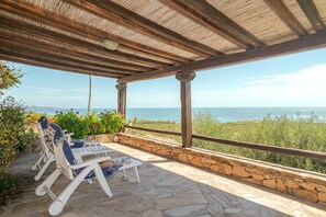 A covered outdoor seating area with stone flooring, wooden beams, and a view of the sea. - Villetta Oleandro with Sea View, Private Terrace and Garden (San Teodoro)