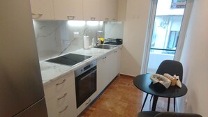 A compact kitchen with white cabinets, a stainless steel refrigerator, a built-in oven, and a black countertop. There is a small dining area with a black table and two chairs. - Seizani Athens Stay: Cozy apartment in welcoming Kesariani (Kesariani, Attiki)