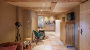 Una habitación acogedora con techo de madera, una zona de comedor con mesa y sillas, un televisor montado en la pared y una cocina al fondo.