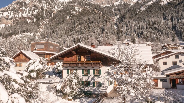 Un edificio de estilo chalete tradicional con techo inclinado, rodeado de árboles nevados y montañas al fondo.