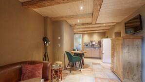 Un espacio de sala acogedor con un sofá de cuero, una pequeña mesa redonda y una silla verde. Se ve un armario de madera al fondo.