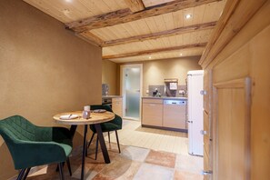 A modern kitchen with wooden beams, a dining area with two green chairs, and a refrigerator.