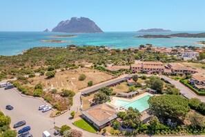 A coastal resort with a swimming pool, villas, and a mountainous backdrop. - Apartment 'Trilocale Corallo 300 Mt Spiaggia' with Shared Pool, Private Terrace and Private Garden (Porto San Paolo)