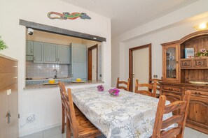 Uma área de refeições com mesa posta para quatro pessoas, cadeiras de madeira, cozinha com armários azul-claros e um aparador de madeira com portas de vidro.
