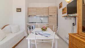 Ett kompakt bostadsutrymme med ett litet kök, ett matbord med stolar, en säng och en TV som är monterad på väggen.