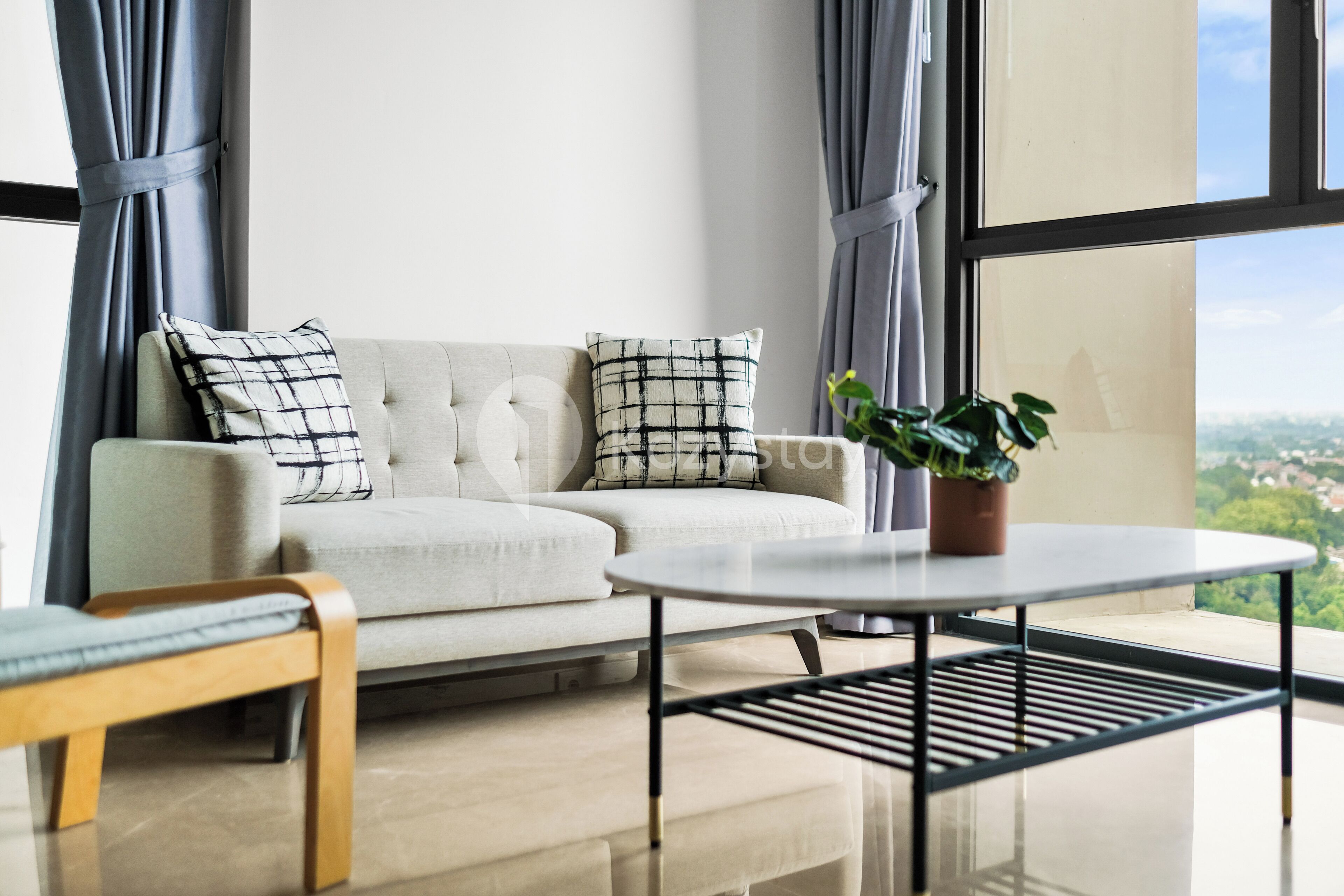 Un salon moderne avec un canapé, deux coussins, une table ronde et une plante en pot.