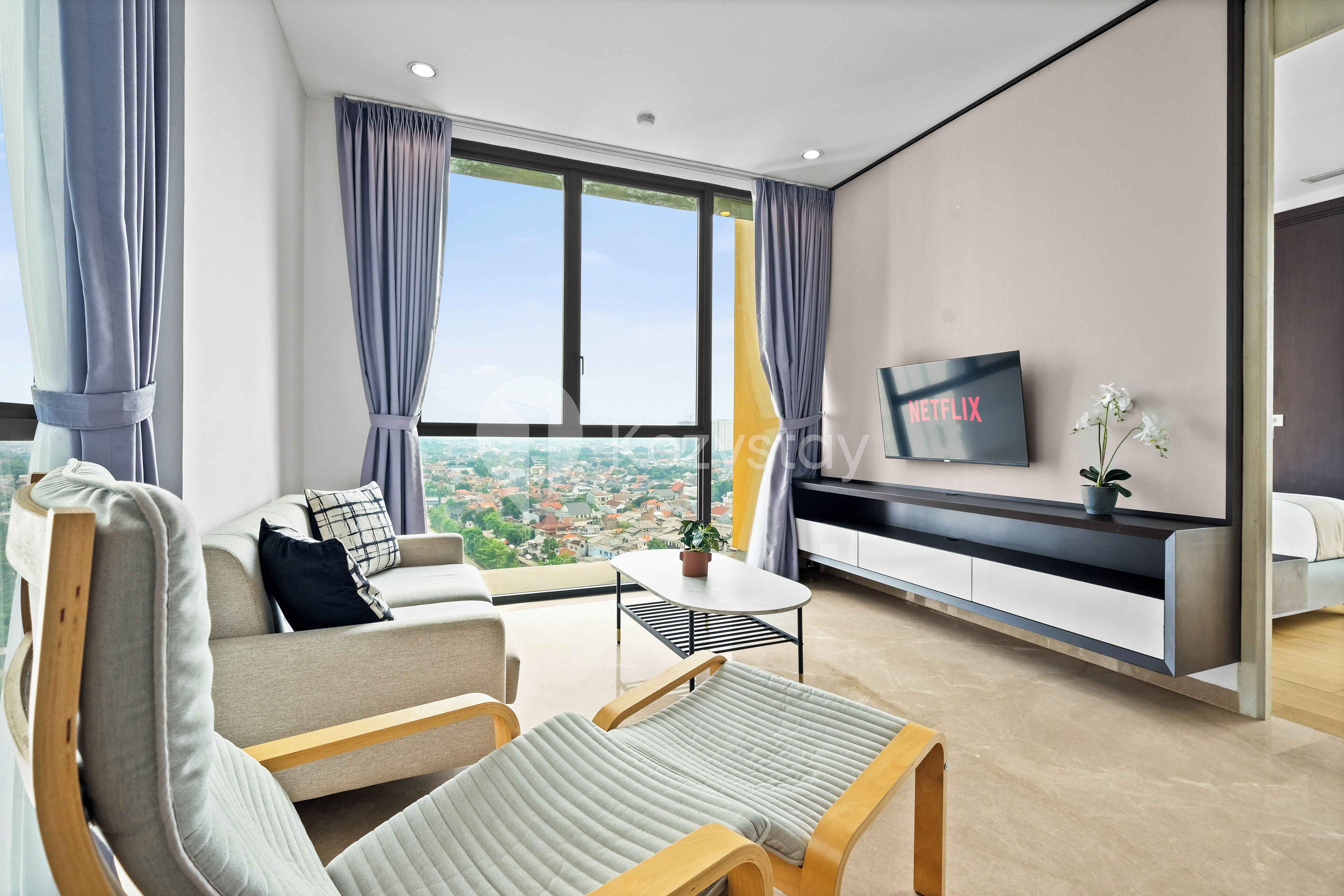 A modern living room with a sofa, two armchairs, a coffee table, and a TV mounted on the wall.