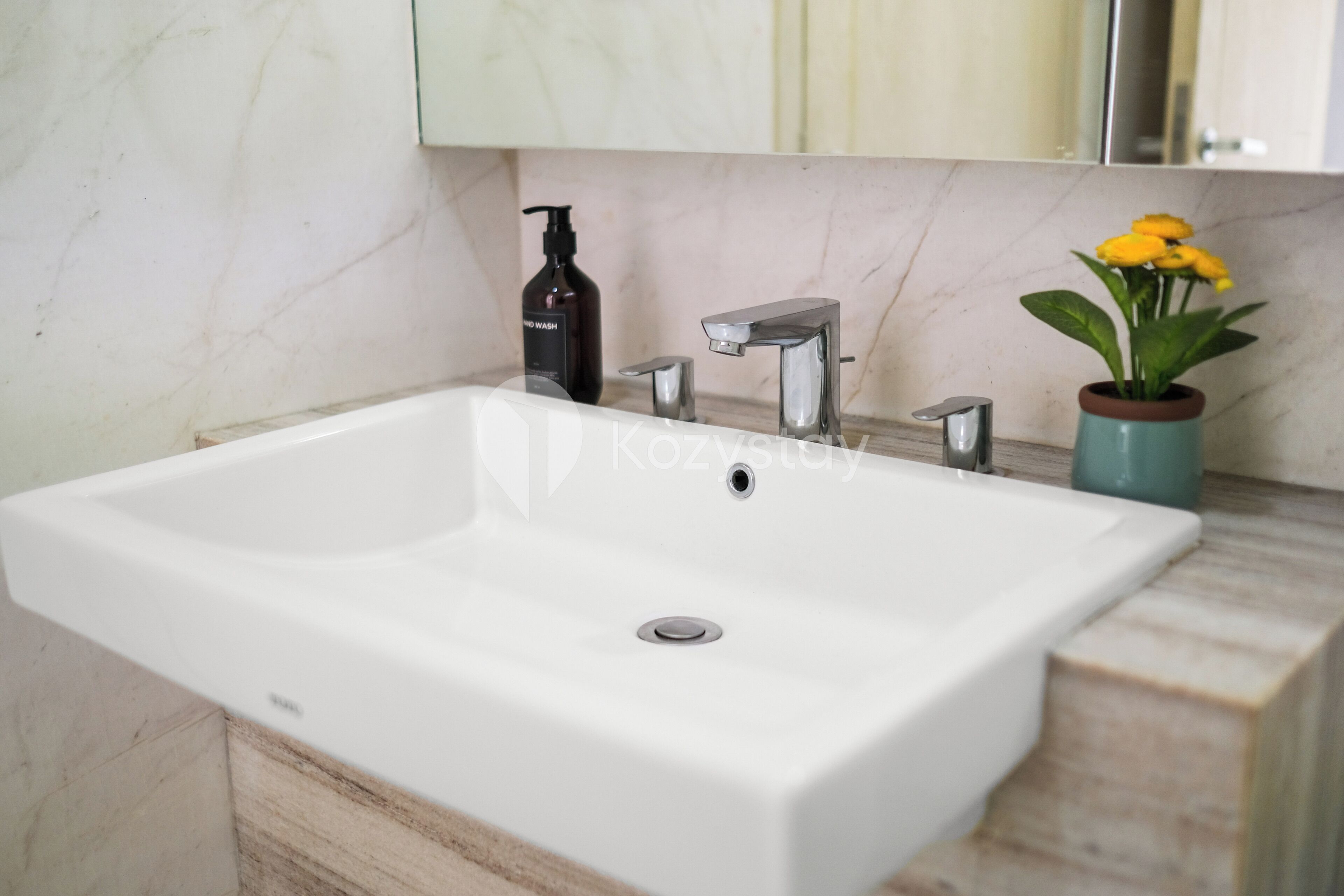 A bathroom with a white sink, a black soap dispenser, a silver faucet, and a vase with yellow flowers on the countertop.