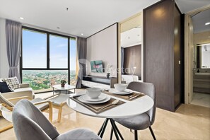 A modern hotel room with a large window, a dining area with a table set for two, and a cozy seating area with a sofa and armchairs. - Arven by Kozystay - Cilandak (Jakarta)