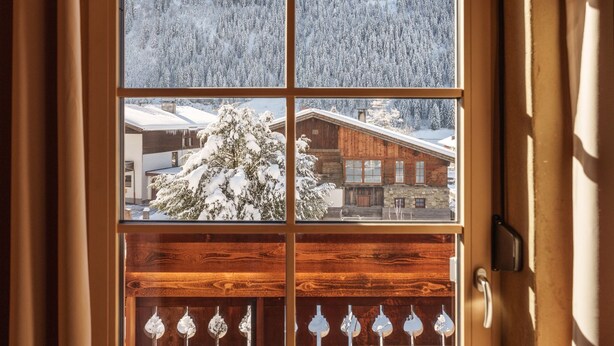 A window with a four-pane view of a snowy landscape, a wooden cabin, and a snow-covered tree. - Klimbim Wohnen und Erleben Annette (Nesselwängle)
