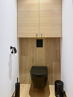 Ein Badezimmer mit Toilette, Mülleimer, Handtrockner und einem Schrank über der Toilette.