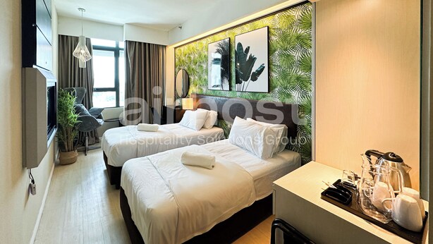 Quarto de hotel com duas camas, uma escrivaninha, espaço para café e uma grande janela com cortinas.