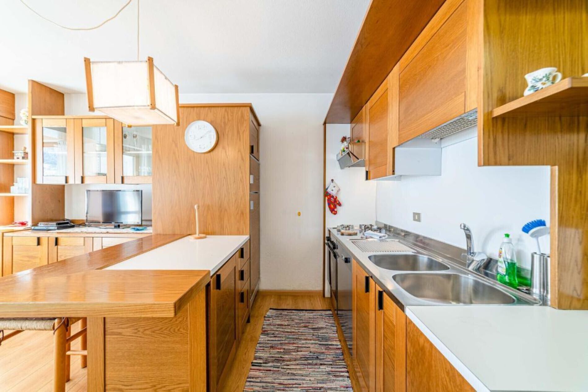 Une cuisine moderne avec des meubles en bois, un grand îlot central, des appareils électroménagers en acier inoxydable et une horloge au mur.