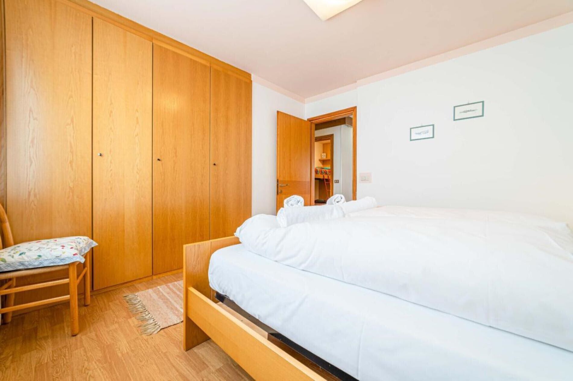 Ein Schlafzimmer mit Holzschrank, einem Einzelbett mit weißer Bettwäsche, einem Holzstuhl und einem kleinen Teppich.