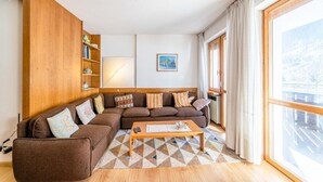 A cozy living room with a brown sectional sofa, a wooden coffee table, and a large window with curtains. - Bernardi Apartment (Caprile)