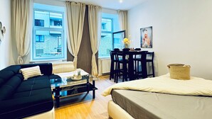 Una stanza moderna e luminosa con un divano, un letto, un tavolo da pranzo e vista su un edificio attraverso ampie finestre.