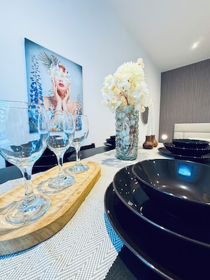 A dining area with a modern table set for two, featuring a glass wine glass, a clear glass, and a black plate. A decorative vase with white flowers is on the table, and a painting is visible in the background. - Comfy 1BR Apt Near Praterstern (Vienna)