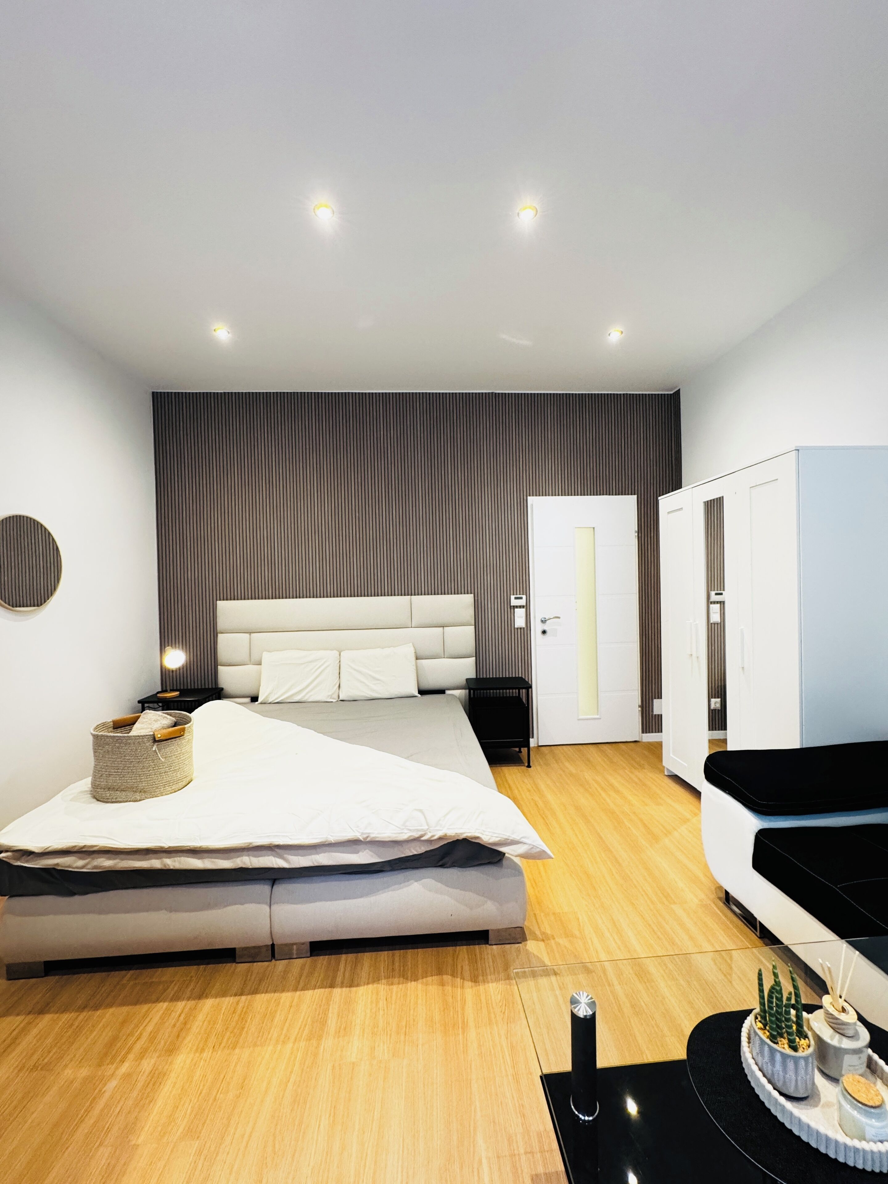 A modern bedroom with a large bed, a wardrobe, and a bedside table with a lamp.