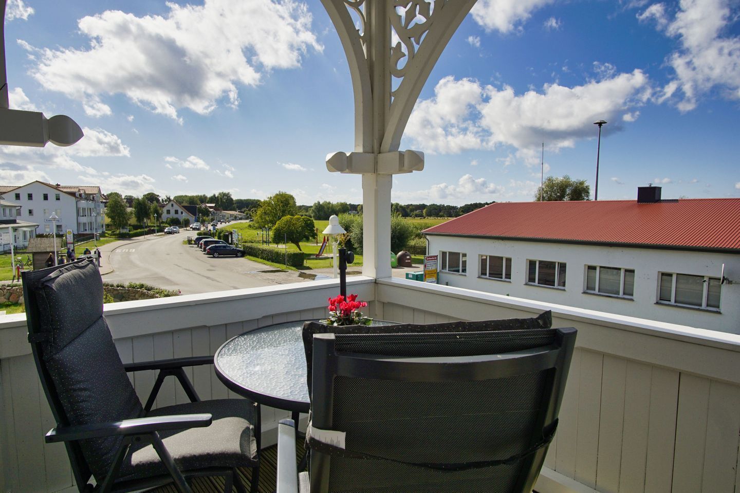 A balcony with two chairs and a table, overlooking a street and buildings.