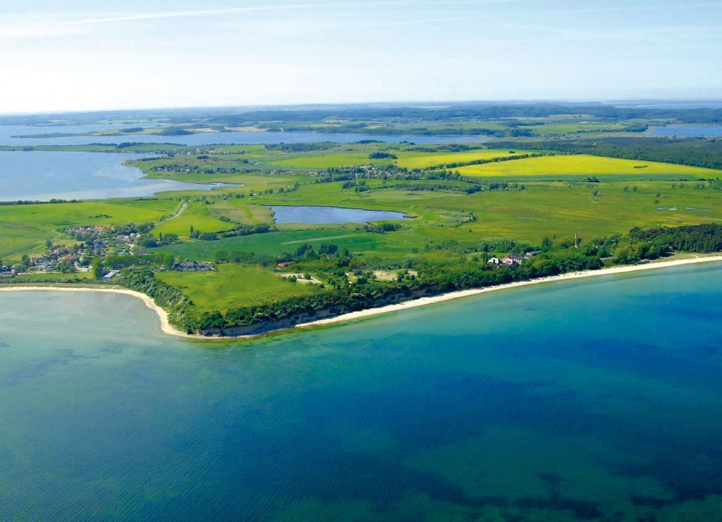 An aerial view of a coastal area with a beach, green fields, and a small town.