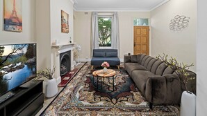 Ein Wohnzimmer mit Flachbildfernseher, Kamin, einer Couch, einem Couchtisch und einem gemusterten Teppich.