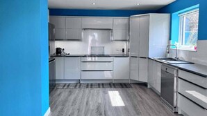 A modern kitchen with grey cabinets, a black countertop, and a stainless steel dishwasher. - The Burghead Hideaway – Calm & Comfort (Burghead)