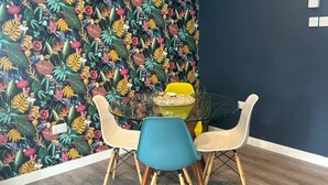 A dining area with a glass table, four chairs, and a tropical-themed wallpaper. - The Burghead Hideaway – Calm & Comfort (Burghead)