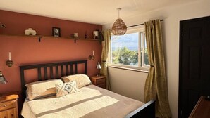 Un dormitorio con una cama grande, cabecera de madera, mesitas de noche, una ventana con cortinas y vistas al exterior.