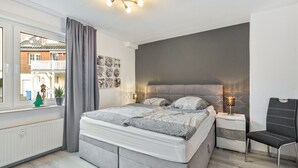 A bedroom with a bed, bedside tables, a chair, a window with curtains, and a view of a building outside. - Apartment 'Hoppernkopf' with Shared Terrace, Private Garden and Wi-Fi (Willingen (Upland))