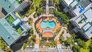Ett flygbildsbild av ett hotellkomplex med en central pool, flera byggnader och välanlagda trädgårdar.