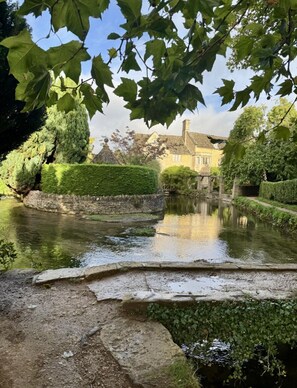 Eine friedliche Flusslandschaft mit einer Steinbrücke, üppigem Grün und einem traditionellen Gebäude im Hintergrund.