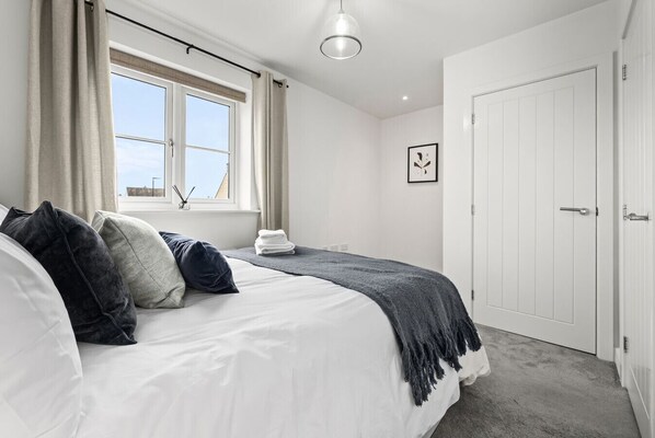A bedroom with a bed, a window, a door, and a framed picture on the wall. - Foxden House – Your Home from Home in the Cotswolds. (Bourton-on-the-Water)