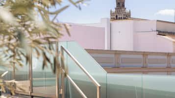 Una escalera conduce a un edificio con una torre del reloj, baranda de cristal y cielo despejado.