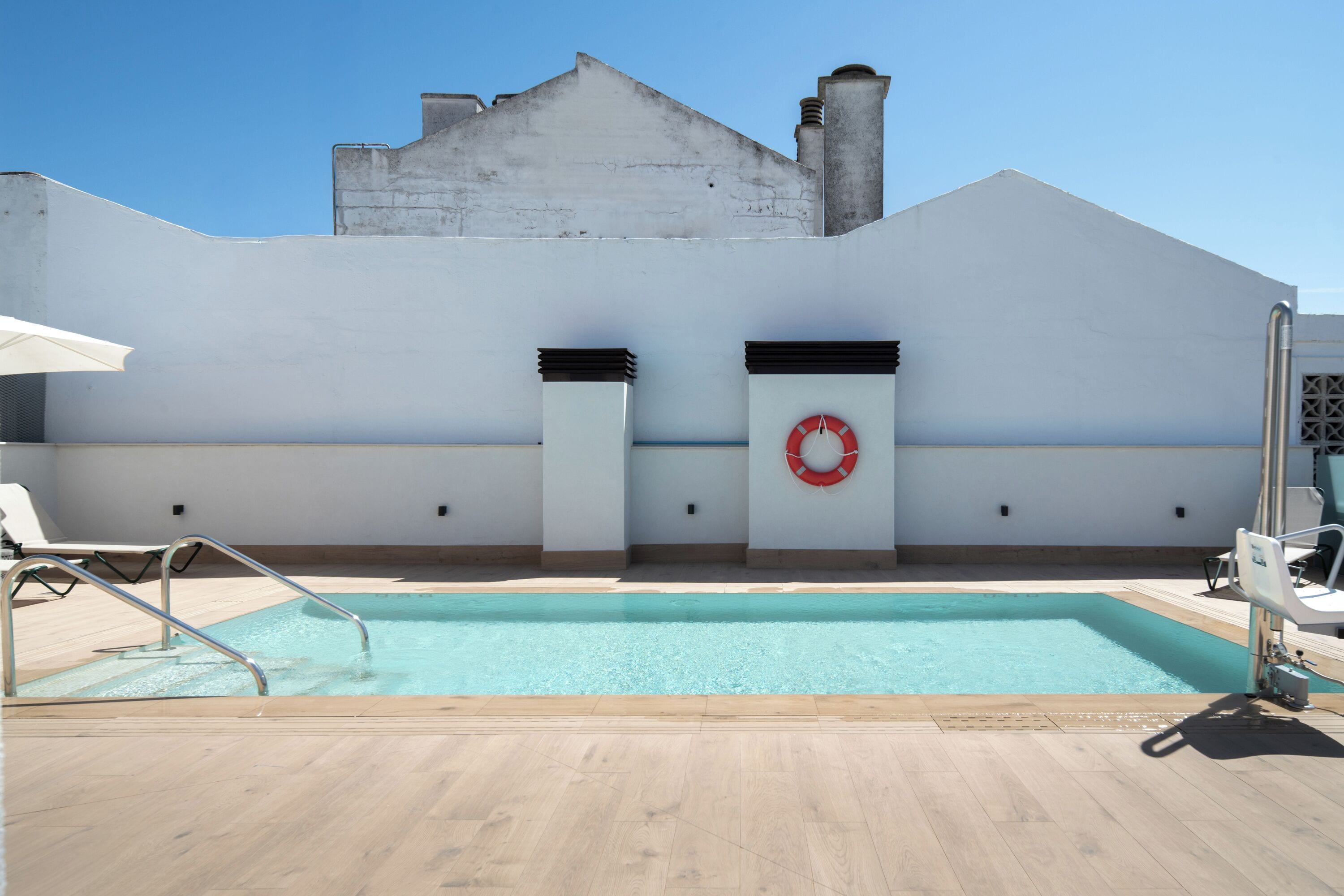 A rooftop pool with a clear blue sky, white walls, and a red lifebuoy.