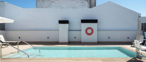 A rooftop pool with a clear blue sky, white walls, and a red lifebuoy.
