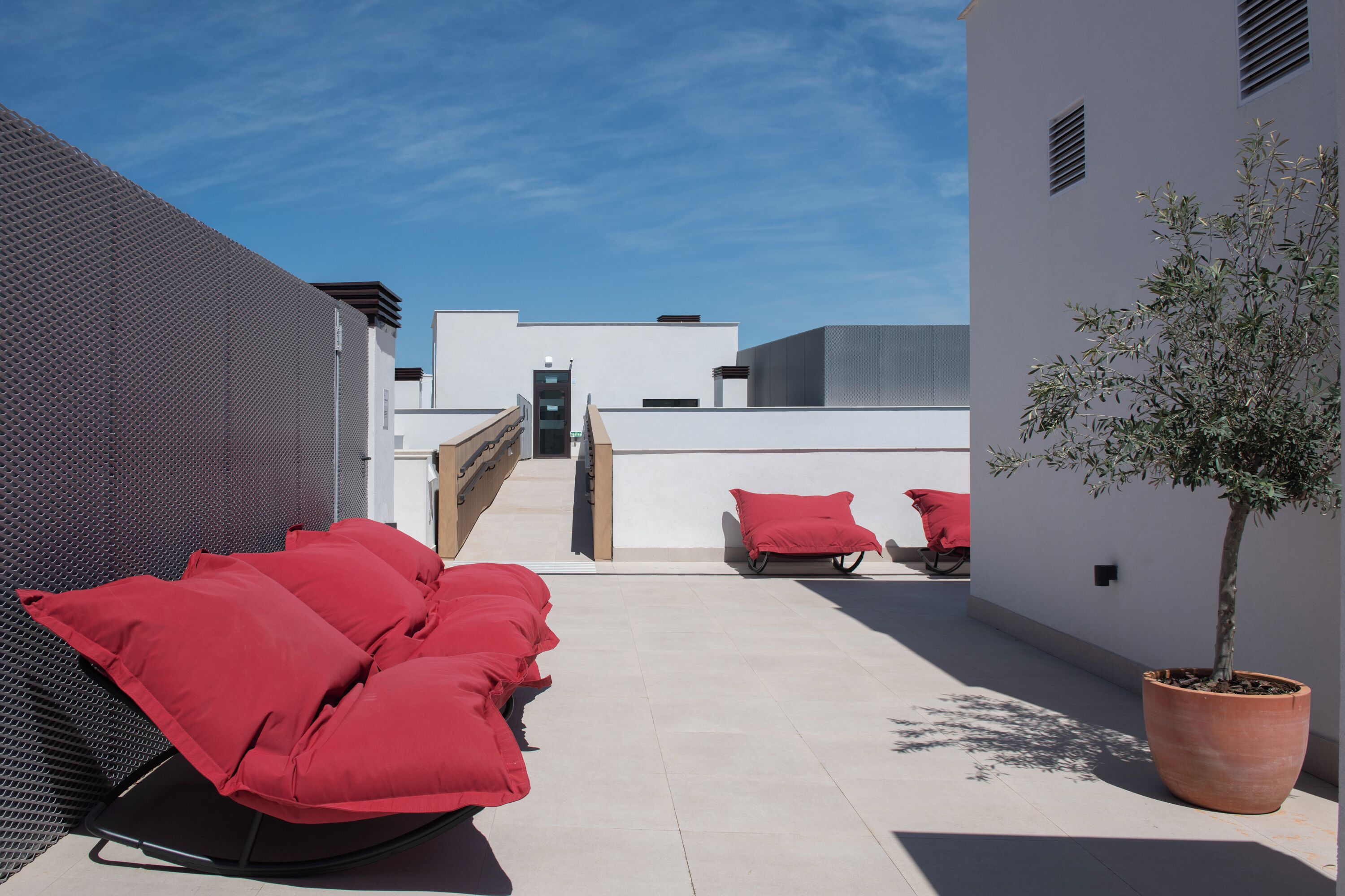 Una terraza en la azotea con asientos acolchados rojos, un árbol en maceta y un cielo despejado.